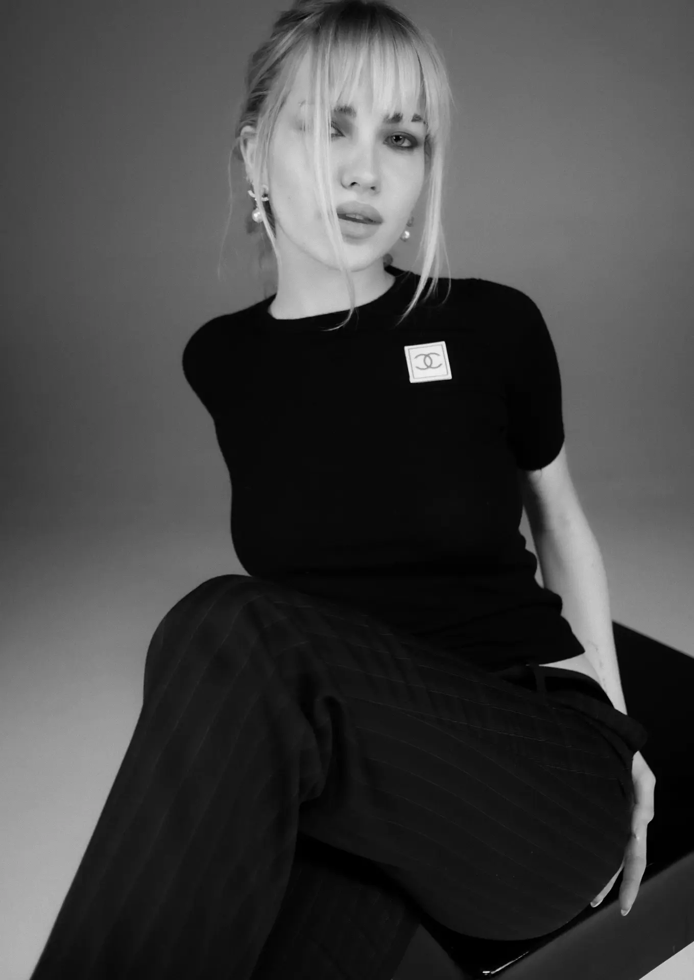 Monochrome studio editorial — model seated in tailored black clothing against a grey field, black and white editorial photography by Maison Division