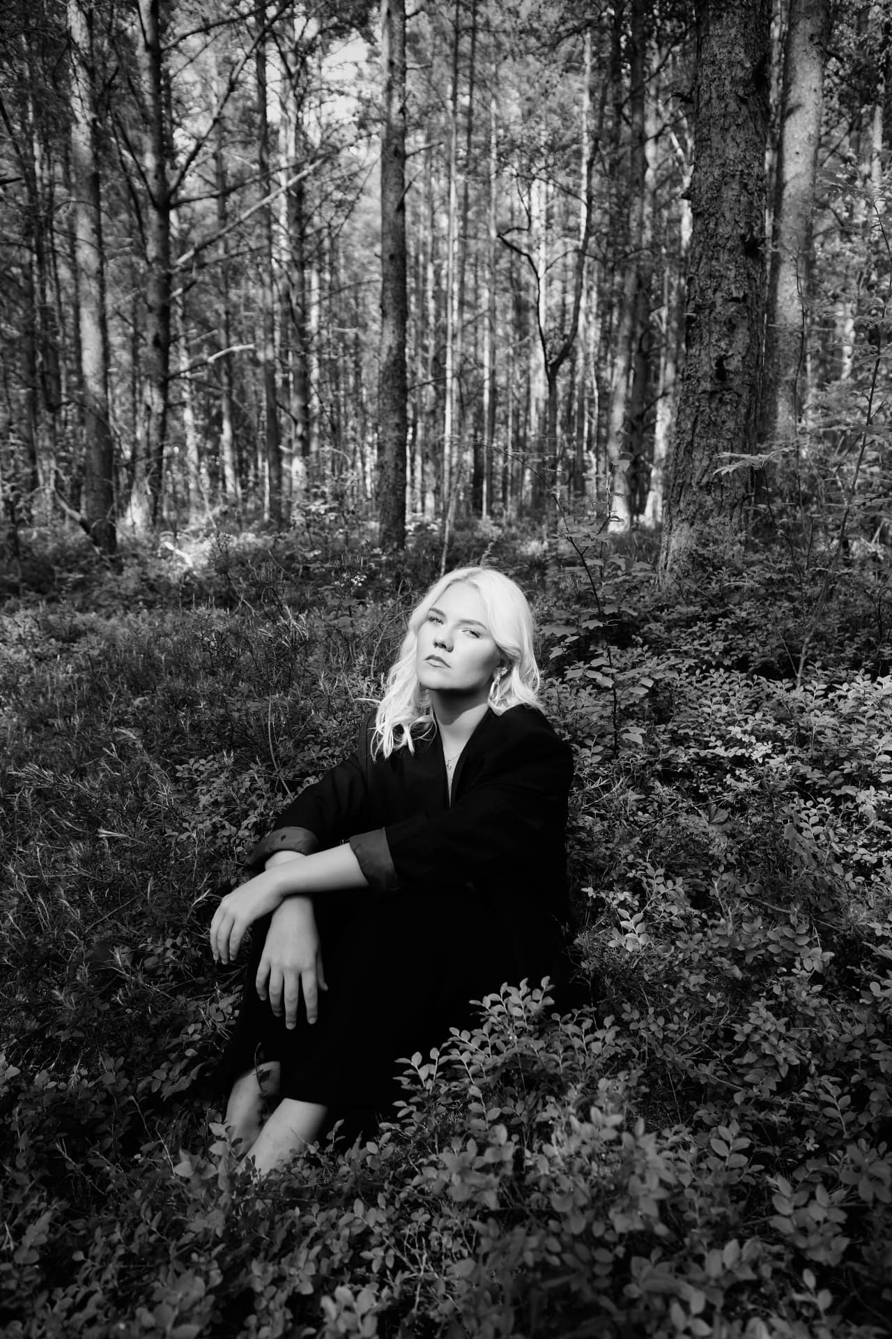 Location portraiture — black and white portrait of a blonde model seated in a pine forest, outdoor editorial photography by Maison Division