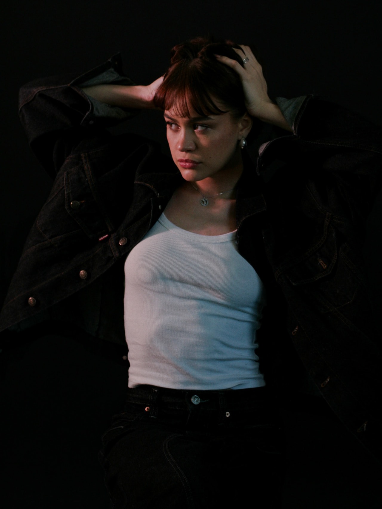 Low-key studio portrait — model in a denim jacket side-lit against a black background, dark studio photography by Maison Division